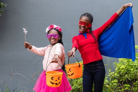 African american girls in superhero cape and tutu trick-or-treating with pumpkin buckets
