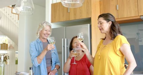 Diverse coworkers toasting with white wine in modern kitchen celebrating teamwork