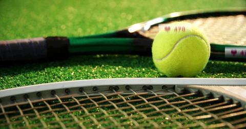 Close-Up of Tennis Ball on Rackets on Green Court Surface