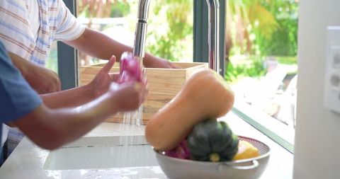 African american father and son washing vegetables at sink, teaching healthy eating habits