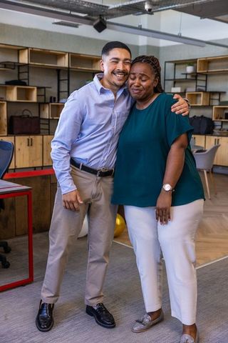 Diverse Coworkers Embracing in Open-Plan Office Show Unity and Teamwork