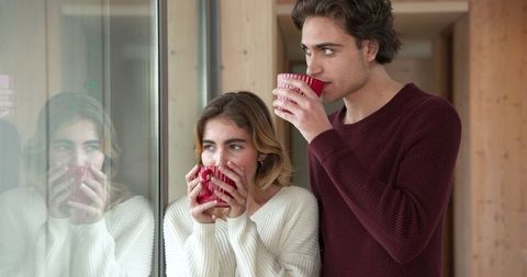 Friends drinking hot beverages by modern window reflection