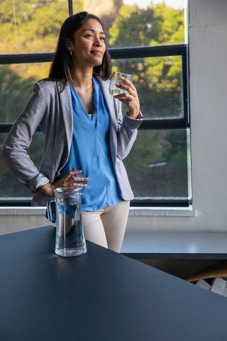 Confident professional woman standing with water glass in modern office