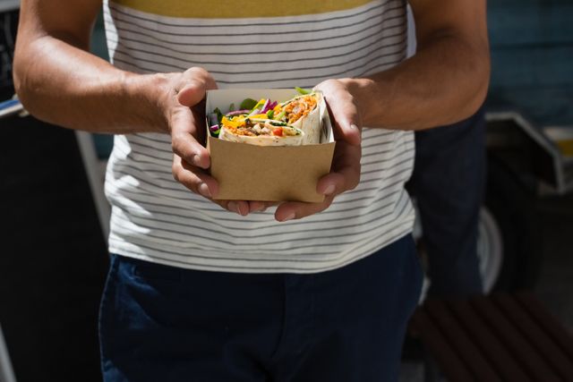 Man holding fresh tortilla wraps in a cardboard box while standing by a food truck. Ideal for use in articles or advertisements about street food, casual dining, food trucks, healthy eating, and outdoor meals.