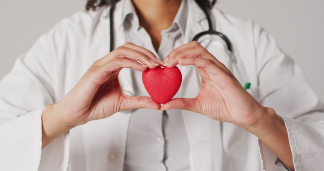 Doctor holding a red heart symbol demonstrating care and awareness about heart health. Image can be used for health-related websites, cardiology promotion, Heart Health Month campaigns, medical articles, wellness programs, and healthcare promotional materials.