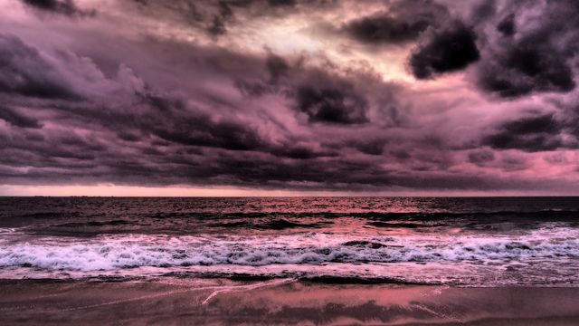 Dramatic view of a sunset over the ocean with stormy, pink-colored clouds. Waves crashing on the shoreline create a mesmerizing and moody scene. Ideal for use in projects related to nature, weather, travel, and coastal living, or as an attractive background or inspirational landscape.