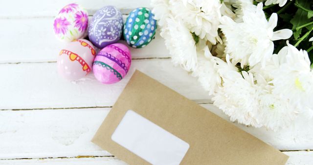 Close-up of multicolored Easter eggs, bunch of flower and envelope on wooden surface
