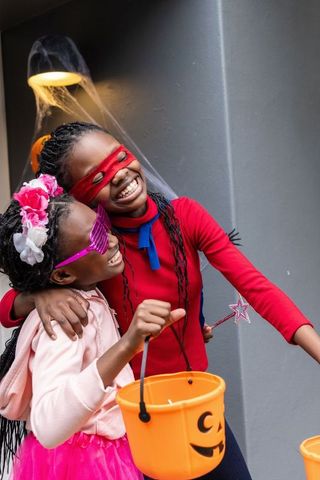 African american girls celebrating halloween in costumes with pumpkin buckets and masks