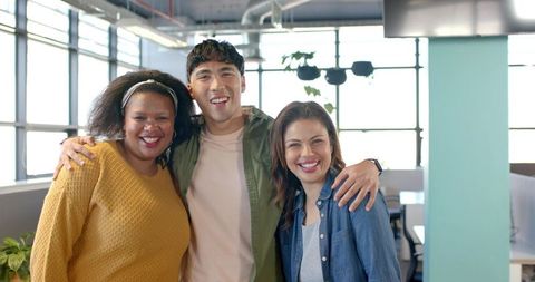 Diverse coworkers smiling and linking arms in sunlit modern open-plan office with plants