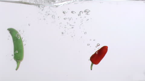 Red and Green Chilis Splashed Underwater in Slow Motion
