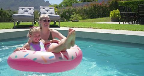 Mother and daughter floating on pink donut pool float smiling in sunny backyard summer