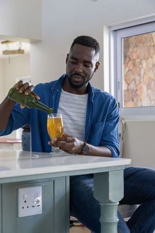 Man Pouring Amber Beverage from Green Bottle into Glass in Kitchen Setting