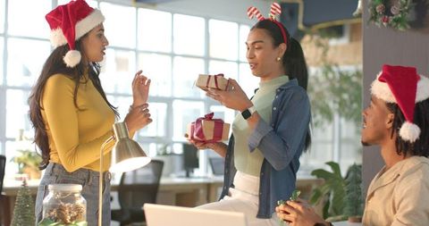 Multicultural office team celebrating holiday party exchanging gifts wearing santa hats