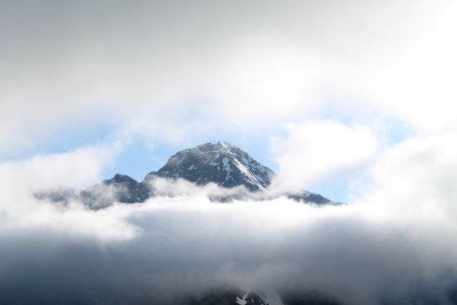 Beautiful image of a snow-capped mountain peak emerging through layers of clouds, showcasing the majestic and serene nature of high altitudes. Perfect for backgrounds, travel promotions, outdoor adventure advertisements, and websites featuring nature and serenity themes.