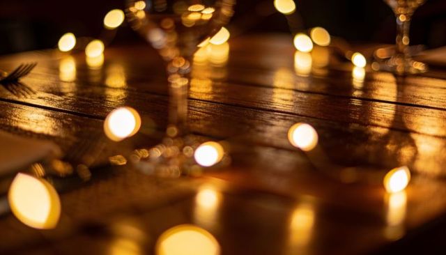 Warm golden fairy lights reflecting on wooden table with wine glass bokeh ambiance