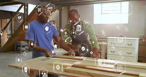 Mature carpenters collaborating in workshop aligning wooden board with digital icons overlay