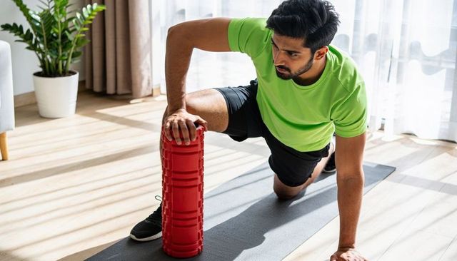 Man using red foam roller during home workout kneeling on exercise mat in sunlit room