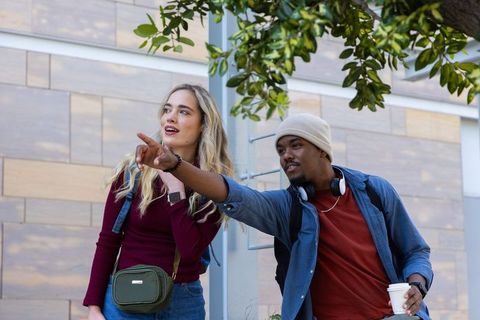 Diverse students pointing and navigating campus route with backpacks, coffee, headphones