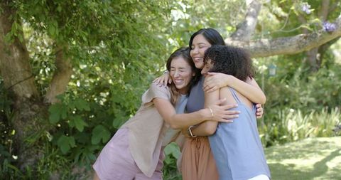 Hugging multiracial friends sharing joyful embrace in sunlit backyard