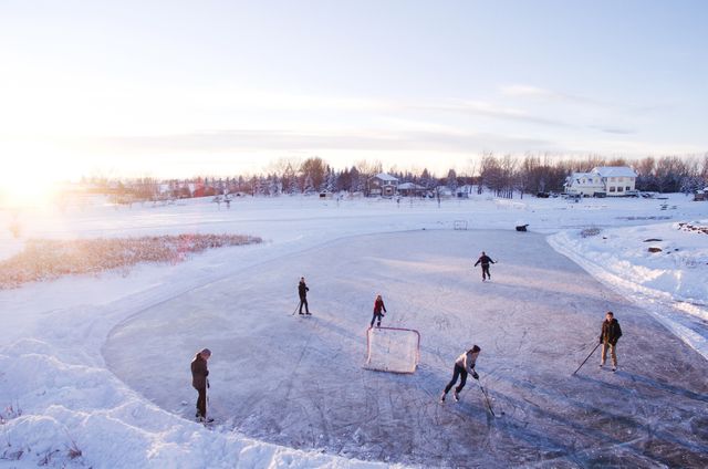 Group of people enjoying an outdoor ice hockey game on a frozen lake during winter at sunset. Perfect for promoting winter sports, recreational activities, seasonal family outings, and community events. Can also be used for content related to leisure activities in cold climates.