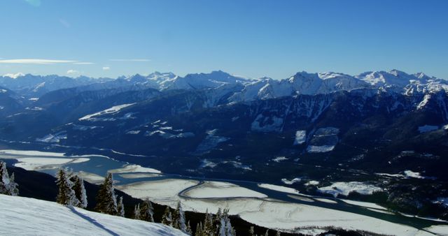 A panoramic view of a snow-covered mountain range with a winding frozen river in the valley, with copy space. Majestic peaks under a clear blue sky offer a serene and breathtaking landscape ideal for winter sports or nature photography.