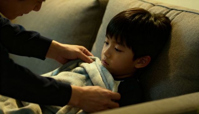 Caregiver tucking child into blanket on couch at night comforting sleepy boy tenderness