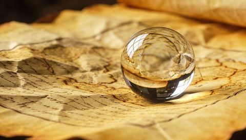 Crystal sphere resting on antique parchment map refracting window light and cartography details