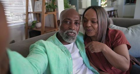 Middle-aged black couple taking cozy living room selfie using smartphone, natural light