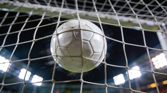 Soccer ball hitting net under stadium floodlights during night rain close-up goal impact