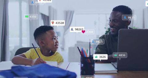 Father guiding son doing homework with laptop and pencil, smiling family learning moment