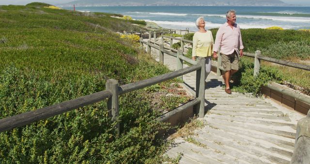 Senior caucasian couple holding hands and walking on path leading to the beach. travel vacation retirement lifestyle