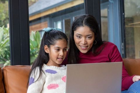 Indian mother and daughter learning together on laptop, cozy family online learning