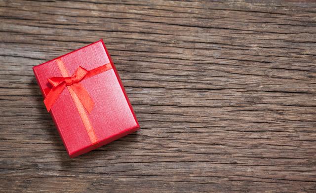 Small red gift box with ribbon placed on wooden surface. Suitable for holiday-themed content, Christmas promotions, gift-giving ideas, festive decorations, and celebration announcements.