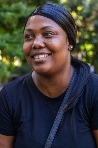African woman smiling outdoors wearing black tee and crossbody strap with stud earrings