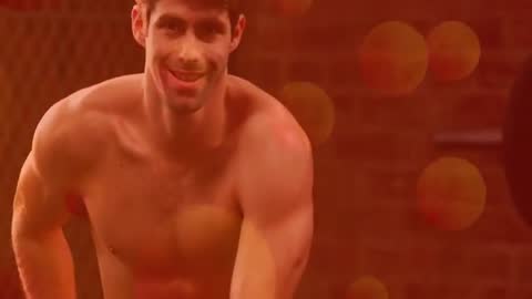 Muscular man warming up in industrial gym, adjusting shorts and smiling in workout video