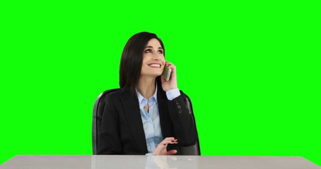 Businesswoman in a suit smiling while talking on phone with green screen background. Useful for illustrating communication and professional settings. Perfect for business-related, corporate, and technology promotions.