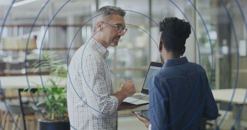 Senior Colleague Guiding Team Member with Laptop and Smartphone in Open-Plan Office