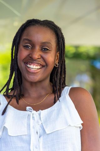 Joyful young woman smiling outdoors in white ruffled top with dreadlocks and gold necklace