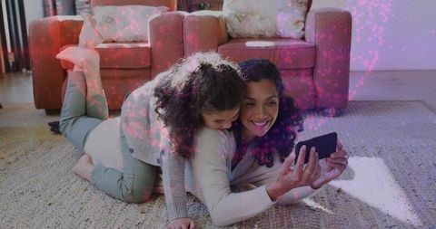 Smiling mother and daughter sharing smartphone on rug, cozy sunlit living room bonding