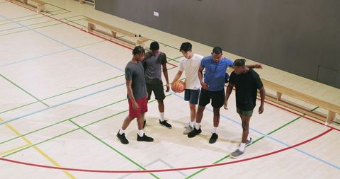 Young multicultural men dribbling basketball and huddling at indoor court showing teamwork
