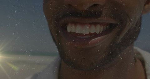 Smiling man showing teeth and jawline at sunlit beach with lens flare and stubble