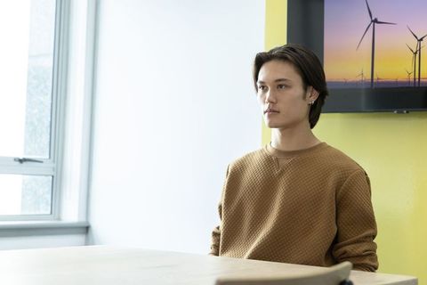 Young asian man sitting in minimal modern office wearing quilted brown sweatshirt