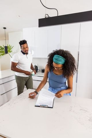 Young couple reviewing documents at modern white kitchen island over morning coffee