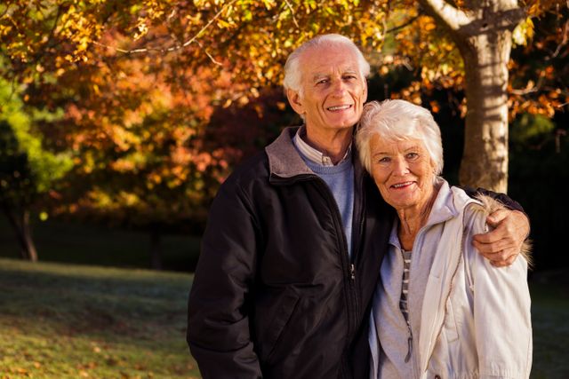 Elderly couple enjoying a moment together in a park surrounded by vibrant autumn leaves. Perfect for themes related to senior lifestyle, retirement, love, outdoor activities, and family bonds.