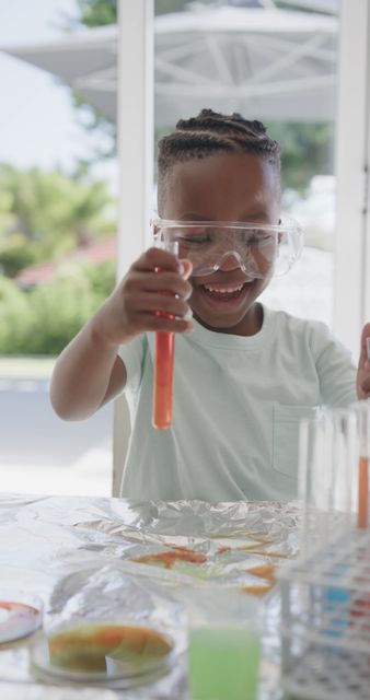 Happy african american boy sitting at table doing chemistry experiments at home. Science, education, childhood and domestic life, unaltered.