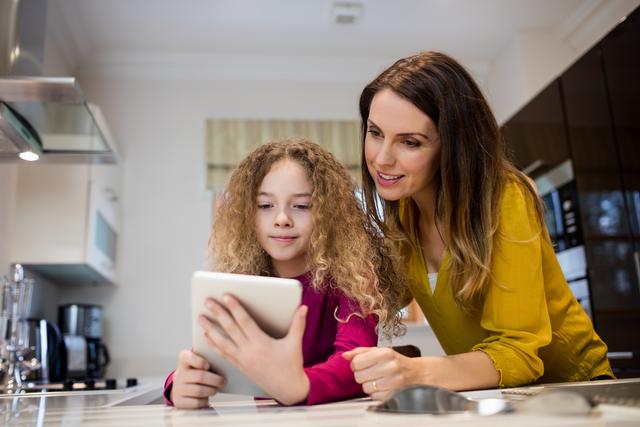 Mother and daughter taking selfie from digital tablet in kitchen at home