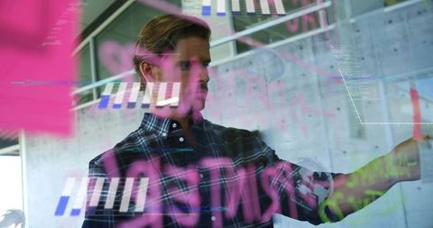 Man writing on glass board with pink overlays in workspace brainstorming and visualization