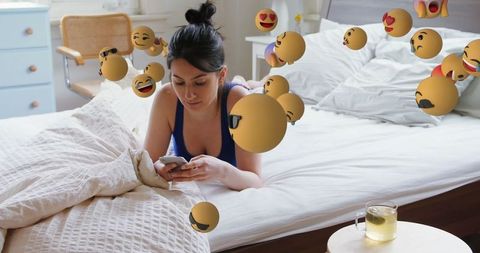 Woman Engaging with Smartphone Amid Emoji Reacts in Bedroom