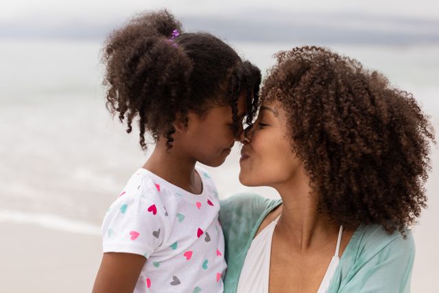 Side view close up of happy young Biracial mother and daughter rubbing noses at beach on a sunny day.