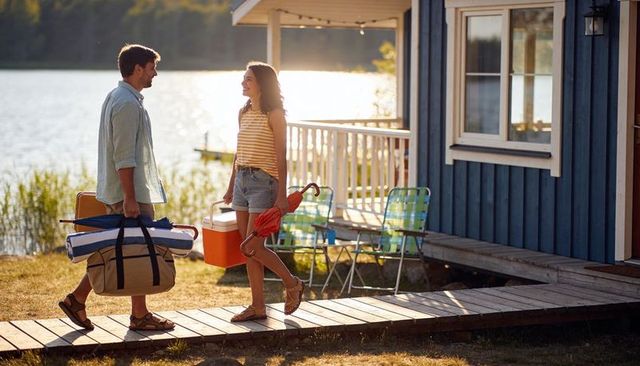 Couple carrying cooler and duffel walking along lakeside cabin boardwalk at golden hour